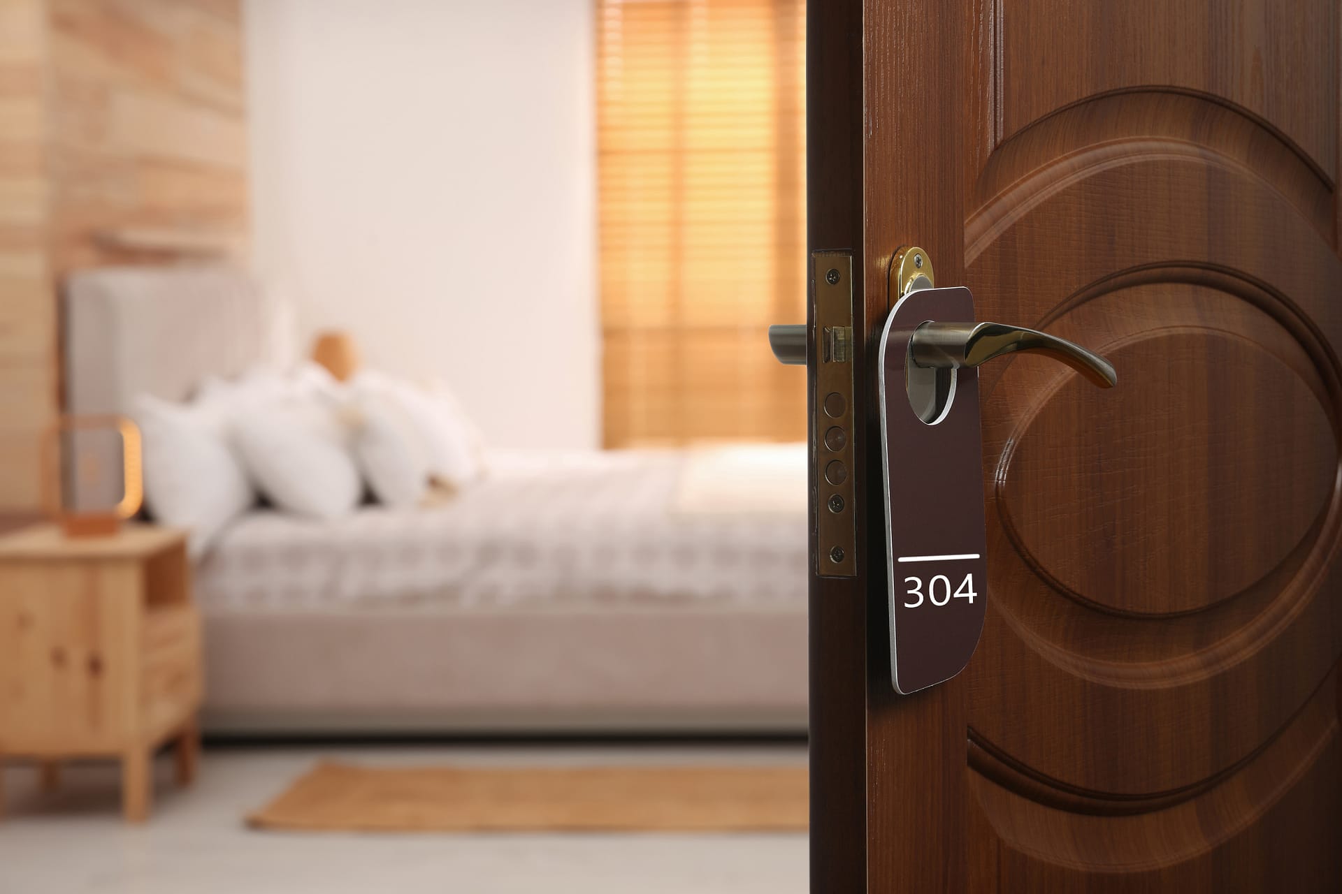 Hotel guest room door with room-number hanger, showing bed and nightstand inside