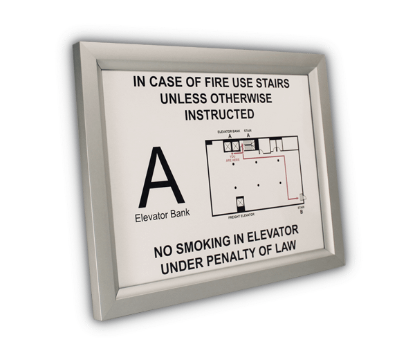 Silver aluminum slide-in frame wall mounted at an angle, showing frame depth and the full evacuation sign