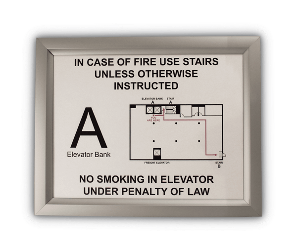 Silver aluminum slide-in frame displaying a New York City elevator landing sign with fire instructions, elevator bank letter, floor plan, and no smoking notice