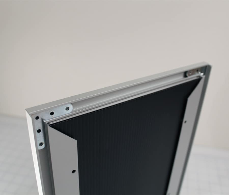 Back of an aluminum slide-in frame showing the open slide rail, pre-drilled wall mounting holes, and black corrugated backing panel